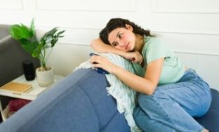 Upset young woman feeling lonely and depressed while sitting on a sofa at home and holding a smartphone; Shutterstock ID 2539602391; purchase_order: Psychologies; job: Digital